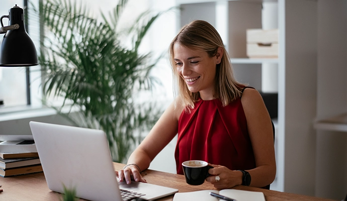 woman wearing red top at desk with laptop and coffee